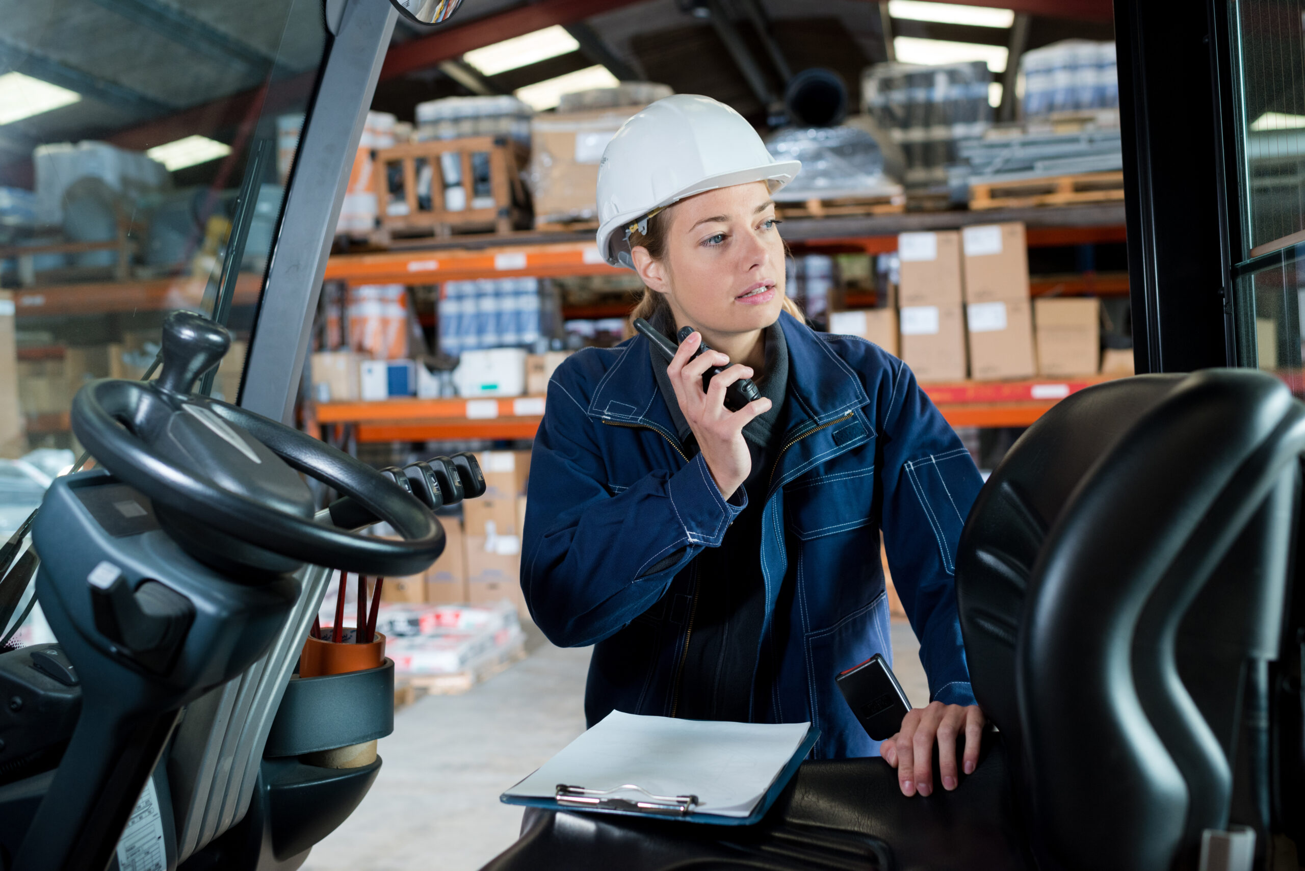 female engineer talking on walkie talkie next to forklift