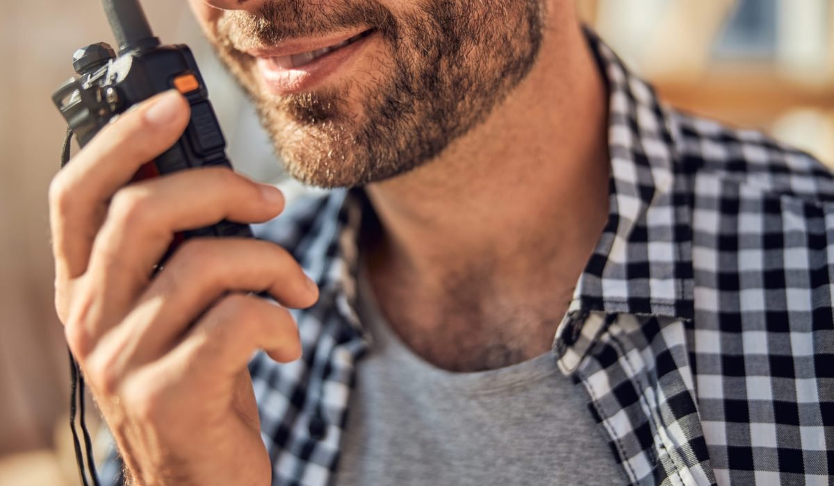 Cropped photo of a bearded young man in a checked shirt holding a walkie-talkie to his mouth
